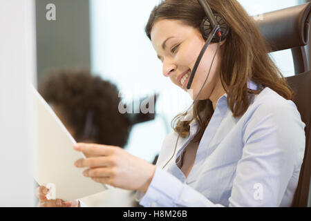 Young businesswoman wearing telephone headset while reading document in office Stock Photo