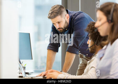 Mid adult businessman using laptop with colleagues wearing headsets in office Stock Photo