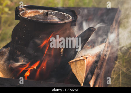 Old used black boiling teapot stands on bonfire, retro stylized photo with tonal correction filter effect, old style Stock Photo