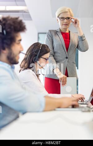 Portrait of confident mature businesswoman with operators working at desk in office Stock Photo