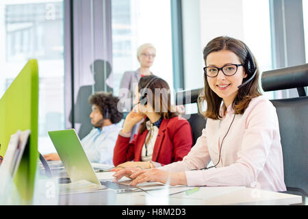 Portrait of smiling customer service representative using laptop while colleagues in background at office Stock Photo