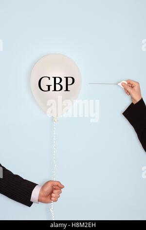 Cropped hands holding needle and popping balloon with text saying GBP Stock Photo