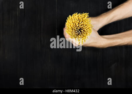 Spaghetti in hands. Top view bunch of raw spaghetti in male hands on black wood vintage table Stock Photo