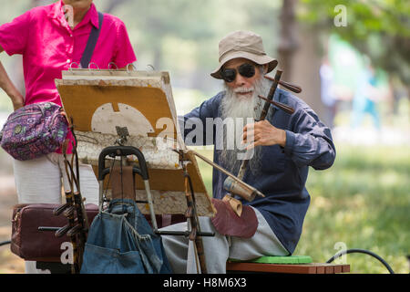 Beijing, China - An elderly Chinese man sitting on a park bench playing the jinghu (violin equivalent in Chinese culture) near t Stock Photo