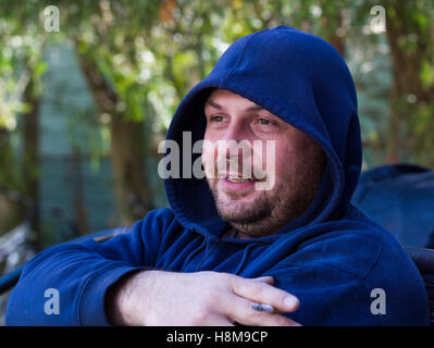 Young man sitting on  chair and  smoking cigarette with hood up. Stock Photo