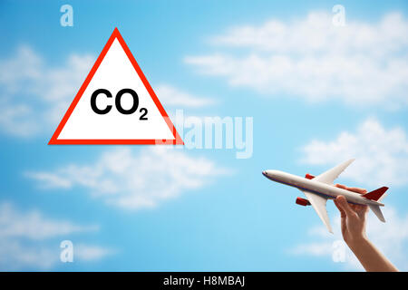 Closeup of woman's hand flying toy plane against cloudy sky with warning CO2 sign Stock Photo