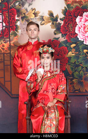 Mixed Race Bride and Groom in Studio wearing traditional Chinese wedding outfits Stock Photo