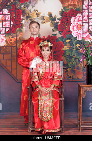 Mixed Race Bride and Groom in Studio wearing traditional Chinese wedding outfits Stock Photo