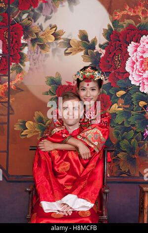 Mixed Race Bride and Groom in Studio wearing traditional Chinese wedding outfits Stock Photo