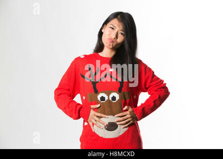 Portrait of woman in Christmas sweater showing she has eaten too much food over gray background Stock Photo