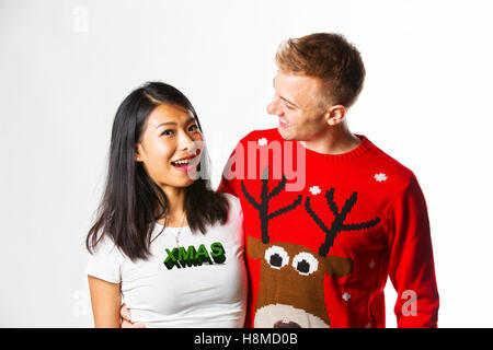 Portrait of happy multi ethnic couple wearing christmas jumpers in studio whilst looking at each other Stock Photo