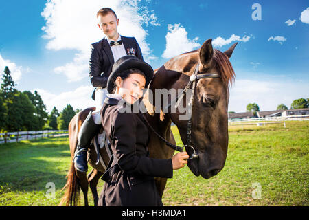 Thoughtful woman standing by man sitting on horse at field Stock Photo