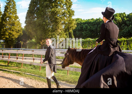 Well-dressed man pulling woman sitting on horse at field Stock Photo