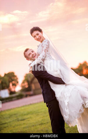 Portrait of happy bridegroom carrying bride on field during sunset Stock Photo