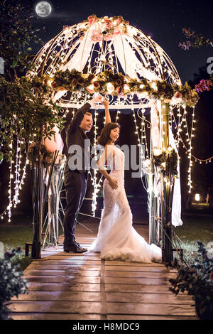 Full length of wedding couple dancing in illuminated gazebo at night Stock Photo