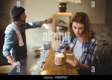 Mechanic using mobile phone while having coffee at counter Stock Photo