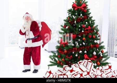 Santa claus with finger on lips standing near christmas tree Stock Photo