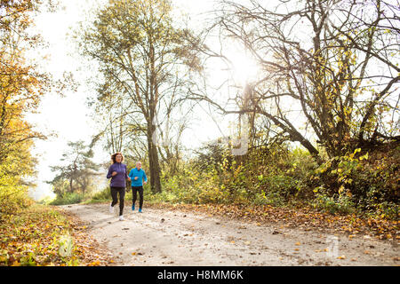 Beautiful senior couple running outside in sunny autumn forest Stock Photo