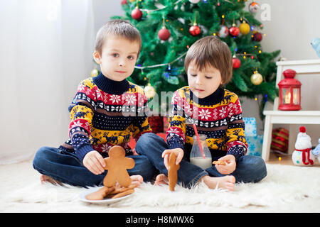 Two adorable children, boy brothers, eating cookies and drinking milk at home, Christmas decoration behind then, kids having fun Stock Photo