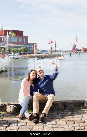 Young couple sitting on promenade and taking selfie with smart phone