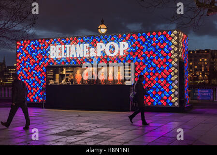 Two bartenders standing behind the counter of an open-air bar on the Southbank as commuters hurry past as night falls. Stock Photo