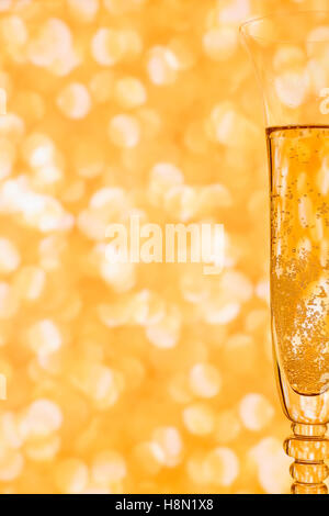 Glass of champagne with sparkles against blurred golden background. Background with copy space Stock Photo