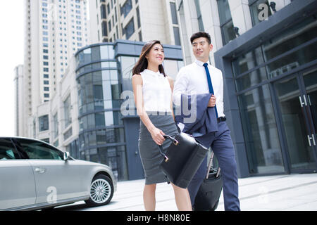 Confident Chinese business people walking with wheeled luggage Stock Photo