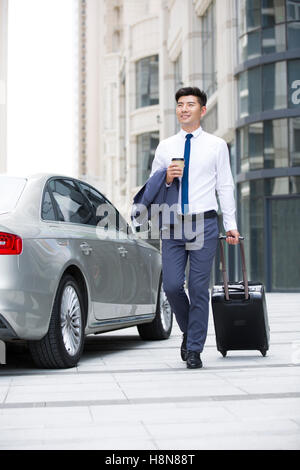 Confident Chinese businessman walking with wheeled luggage Stock Photo