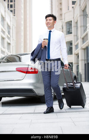 Confident Chinese businessman walking with wheeled luggage Stock Photo