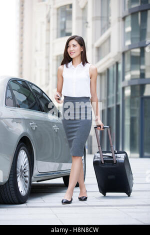 Confident Chinese businesswoman walking with wheeled luggage Stock Photo