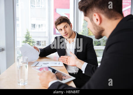 Two young businessmen discussing business plan and using tablet in office Stock Photo