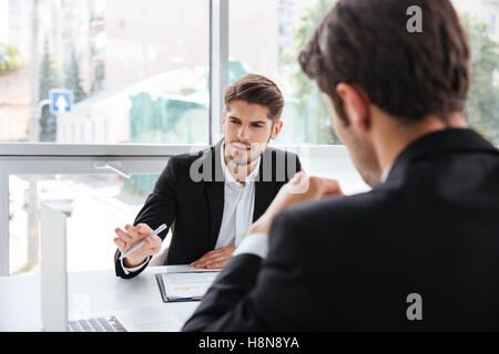 Two concentrated young businessmen working with laptop in office Stock Photo
