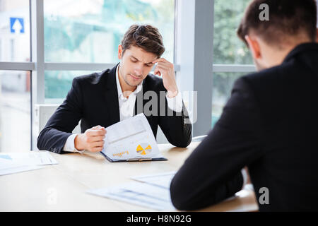 Two thoughtful young businessmen working with business plan in office Stock Photo
