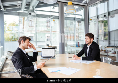 Two happy young businessmen sitting and working together on business meeting Stock Photo