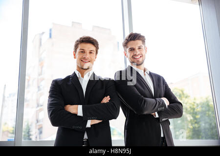 Two happy confident young businessmen standing with arms crossed in office Stock Photo