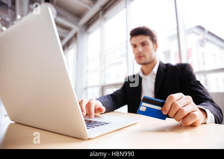 Serious young businessman using laptop and credit card in office Stock Photo