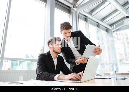 Two serious young businessmen using laptop and tablet in office together Stock Photo