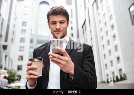 Confident young businessman using cell phone and drinking coffee in the city Stock Photo