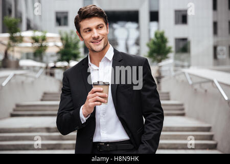 Happy attractive young businessman smiling and drinking coffee in the city Stock Photo