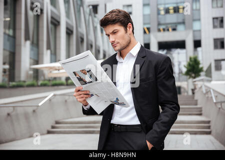 Concentrated young businessman standing and reading newspaper outdoors Stock Photo