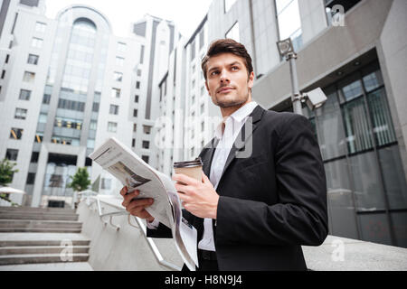Handsome young businessman reading newspaper and drinking coffee in the city Stock Photo