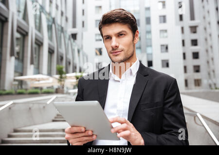 Pensive handsome young businessman using tablet in the city Stock Photo