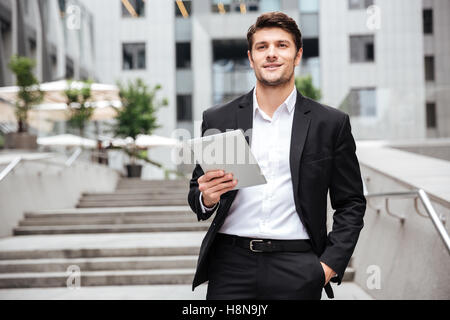 Happy confident young businessman with tablet walking in the city Stock Photo