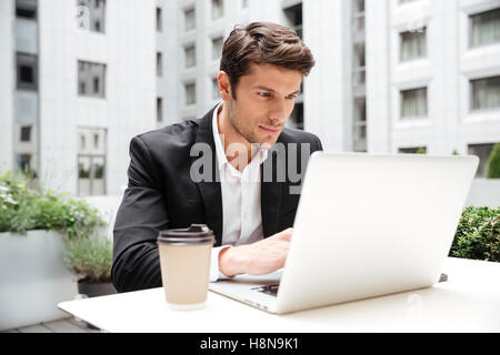 Concentrated young businessman using laptop in outdoor cafe Stock Photo