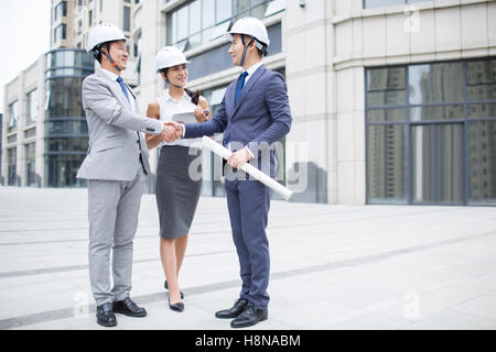 Confident Chinese architects shaking hands outdoors Stock Photo
