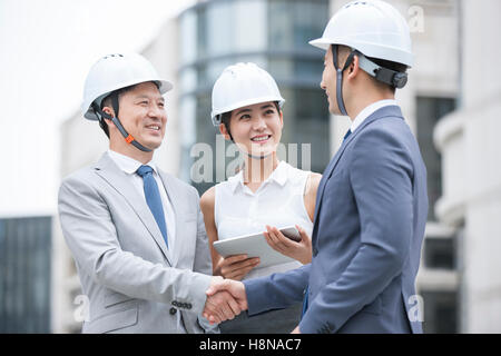 Confident Chinese architects shaking hands outdoors Stock Photo