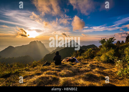 Two hikers enjoying sunrise from top of a mountain Stock Photo