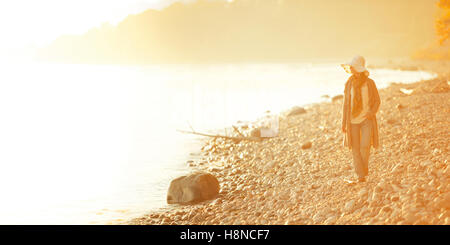 Woman walking along rocky shore at sunset Stock Photo