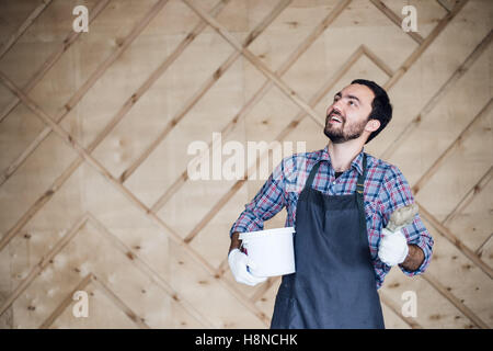 Man with tin of paint and brush looking up on a wooden wall background. Copy space for your text Stock Photo