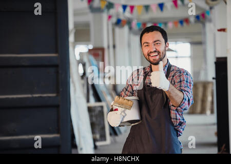 Handyman using brush in his workshop with thumb up Stock Photo